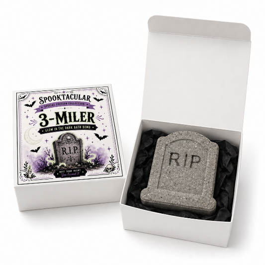 A Halloween-themed bath bomb set shown in its packaging, featuring a gray tombstone-shaped bath bomb with 'RIP' engraved inside an open white box, alongside the illustrated product box labeled 'SPOOKTACULAR 3-MILER'.
