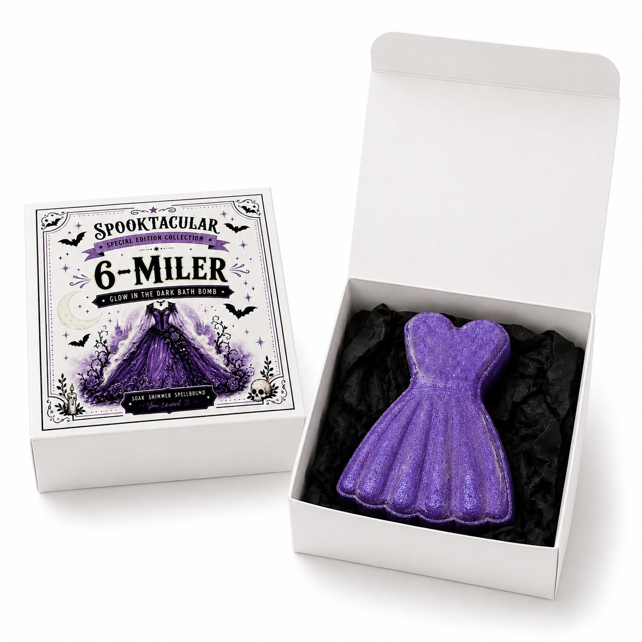 A purple glittery dress-shaped bath bomb displayed in an open white gift box with black tissue paper, alongside the branded lid artwork that reads 'SPOOKTACULAR 6-MILER'.